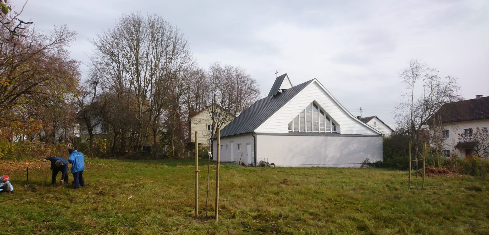 Friedenskirche, im Vordergung Bäume, links BNler, die mit Pflanzen beschäftigt sind